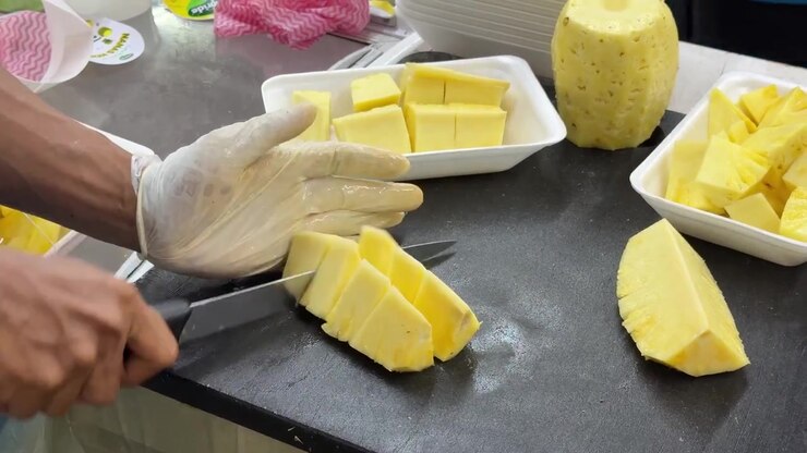 Worker Slicing Fresh Pineapple into Pieces on Cutting Board
