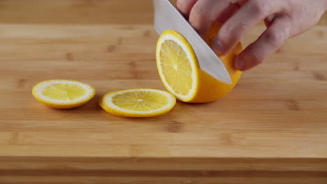 hands slicing a piece of juicy lemon on the wooden chopping board with a sharp knife - close up