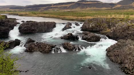 the less crowded but beautiful waterfall glanni surrounded by a magical icelandic landscape with lush green bushes and majestic mountains in the background