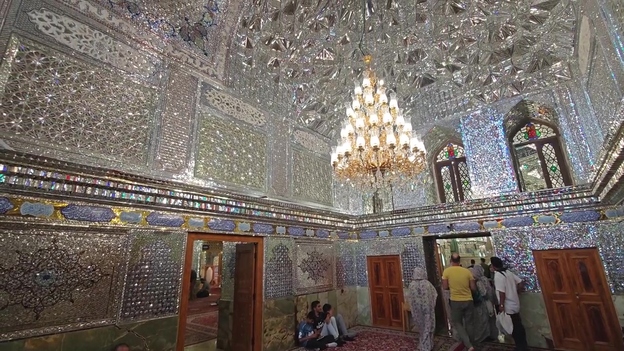 Persone che visitano l'interno specchiato e riccamente decorato di una storica moschea persiana