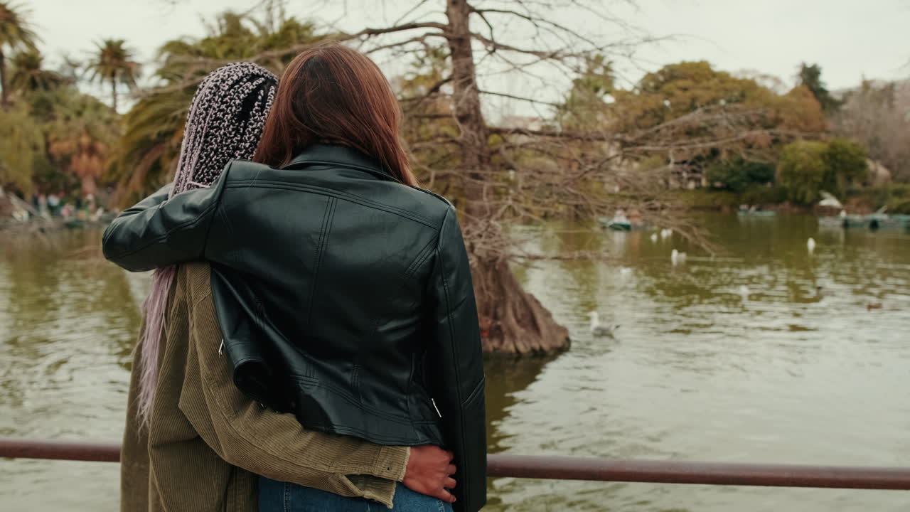 Two Young Women Embracing by a Lake in a Park