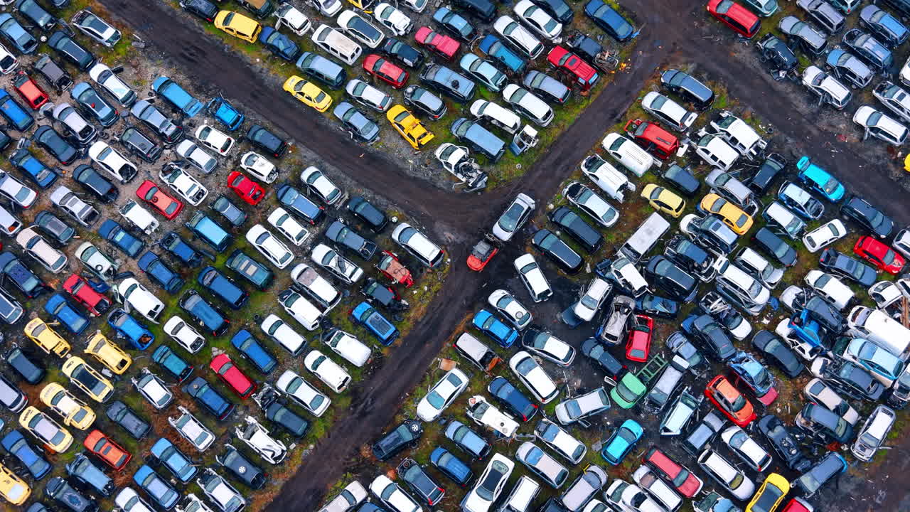 Luftfoto af organiserede rækker af biler på en skrotplads. Droneoptagelse ovenfra af forskellige farvede beskadigede biler parkeret på et industrielt bilgenbrugsanlæg.
