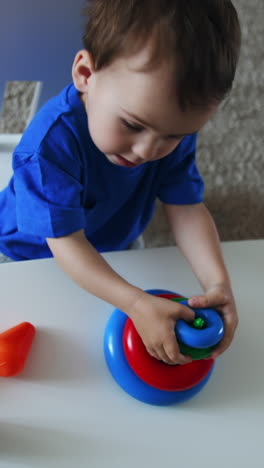dark-haired caucasian child assembling toy pyramid. charming kid plays sitting at desk indoors. top view. vertical video