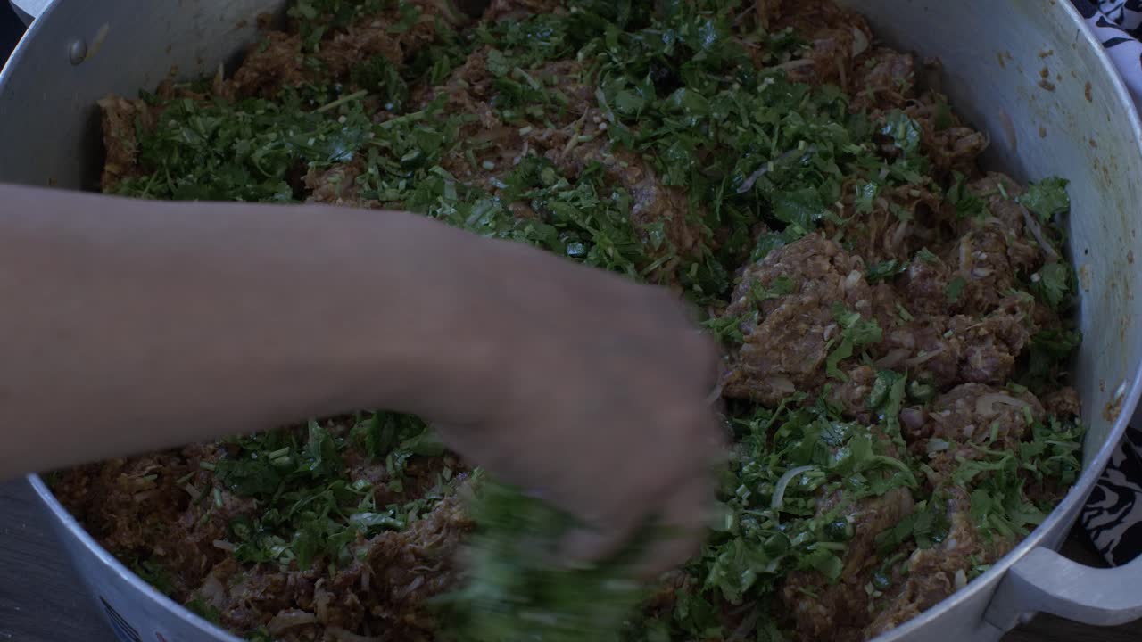 hembra rociando con la mano cilantro fresco sobre carne picada en una sartén grande