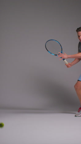 vertical video studio shot of male tennis player returning shot in match hitting ball with racket against grey background