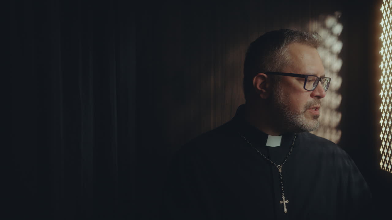 Catholic Priest Speaking to Penitent from inside of Confessional Booth