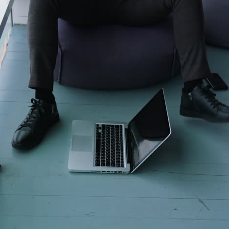 laptop on floor in office. legs of a businessman near the modern gadget. man trying to press on the laptop by foot while sitting in the office by the window. close-up