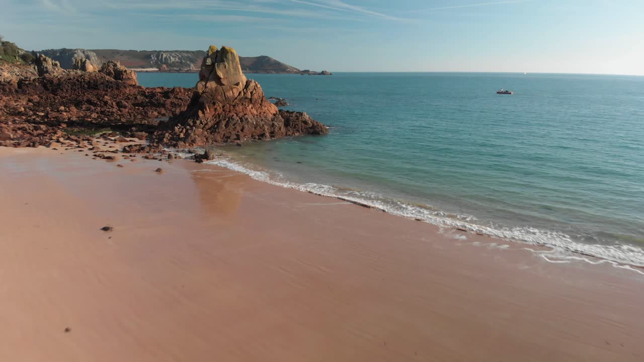 Plano aéreo de uma praia arenosa com rochas, avançando perto de um barco.
