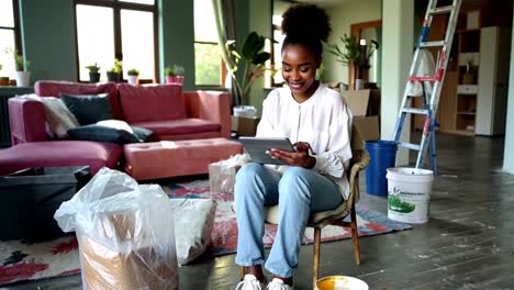 a woman is sitting in a chair in a living room, looking at a tablet