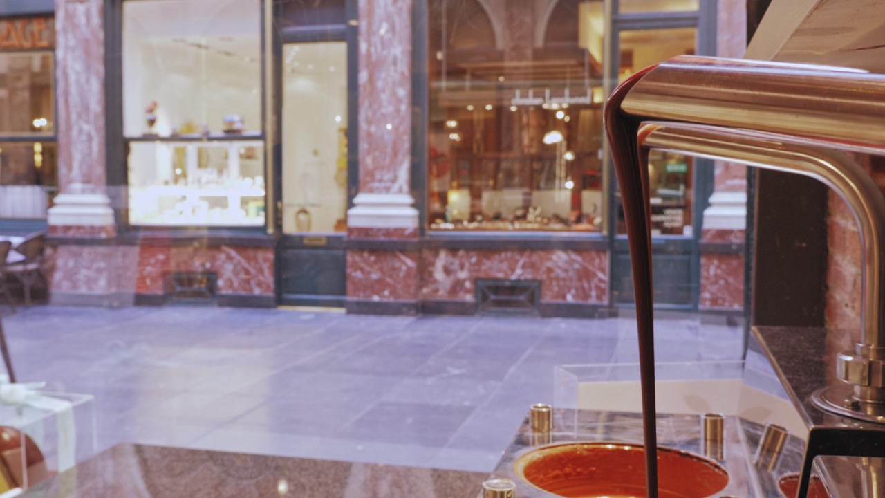 Flowing melted chocolate display in elegant Brussels shop window overlooking marble-clad street.