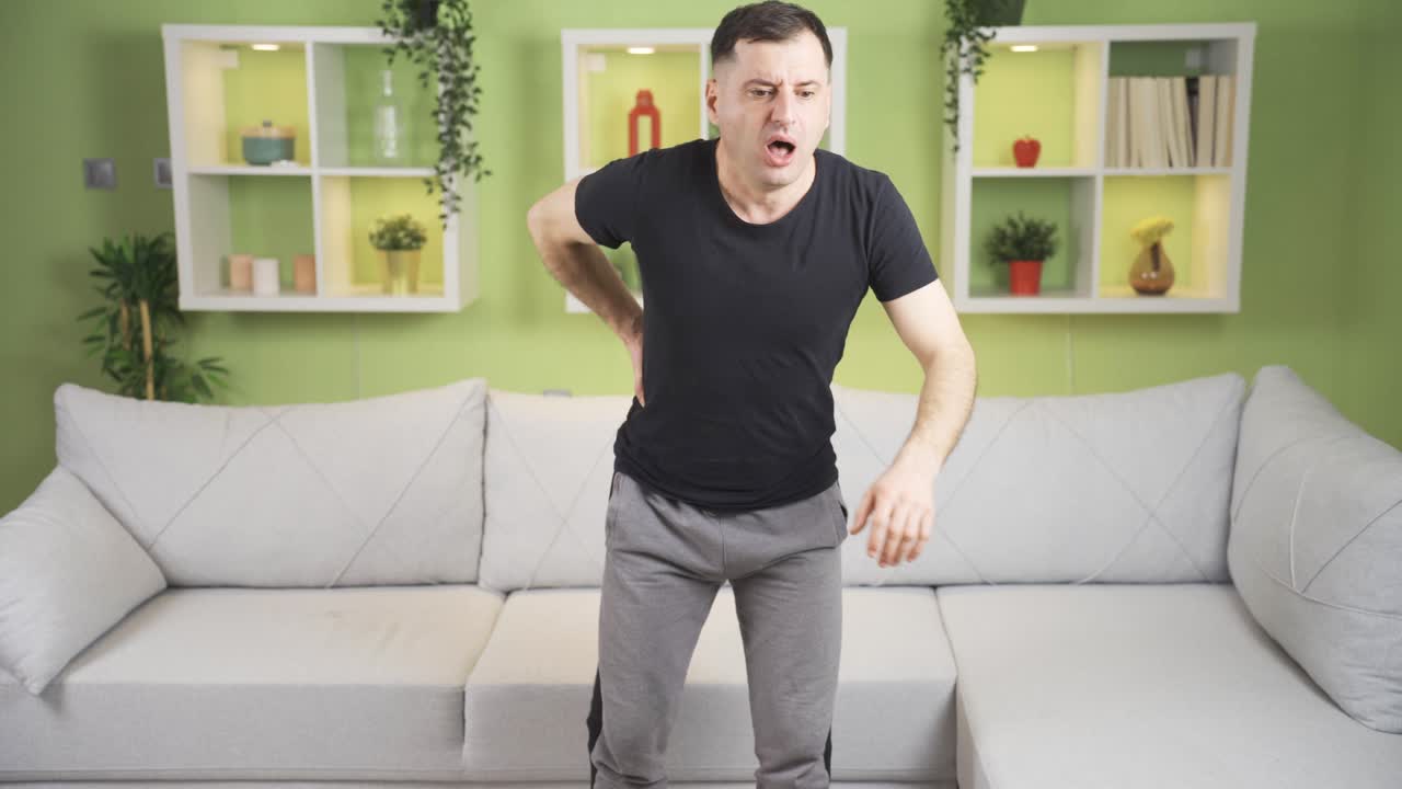 슬픈 성인 남자가 소파에서 일어나면서 허리 통증을 느끼고, 피곤한 남자가 척추를 만지고 있습니다.