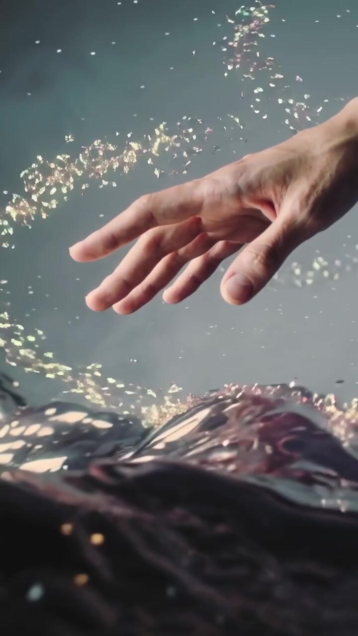 Vertical video: Reacting to rising golden ribbon, right hand reaching toward dark water, copy space