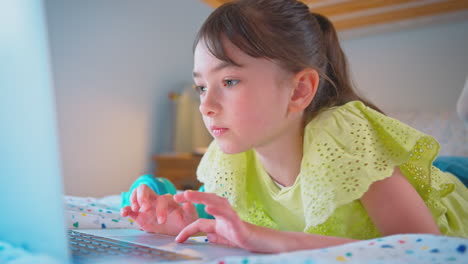 chica en el dormitorio acostada en la cama usando la computadora portátil para hacer la tarea