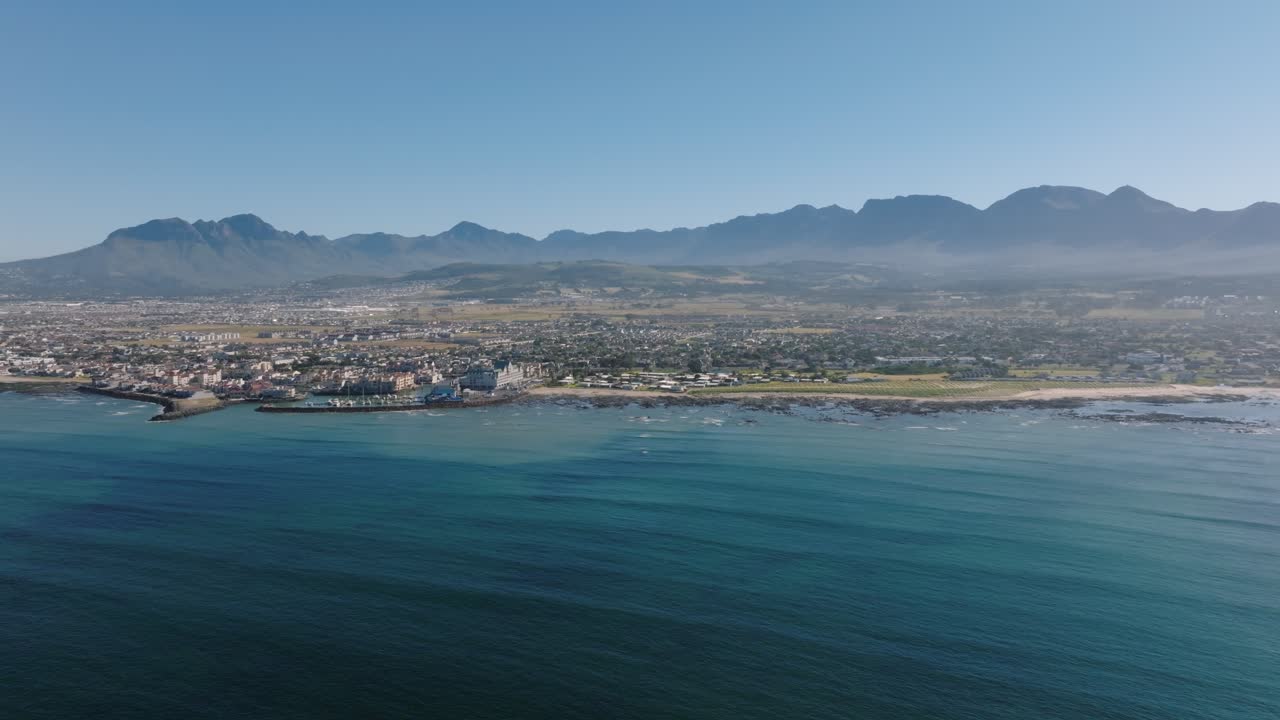 Gordon Bay City with port and mountains in distance. Harbor City in Suburb of Cape Town. Aerial approaching wide shot. Sunny day in South Africa.