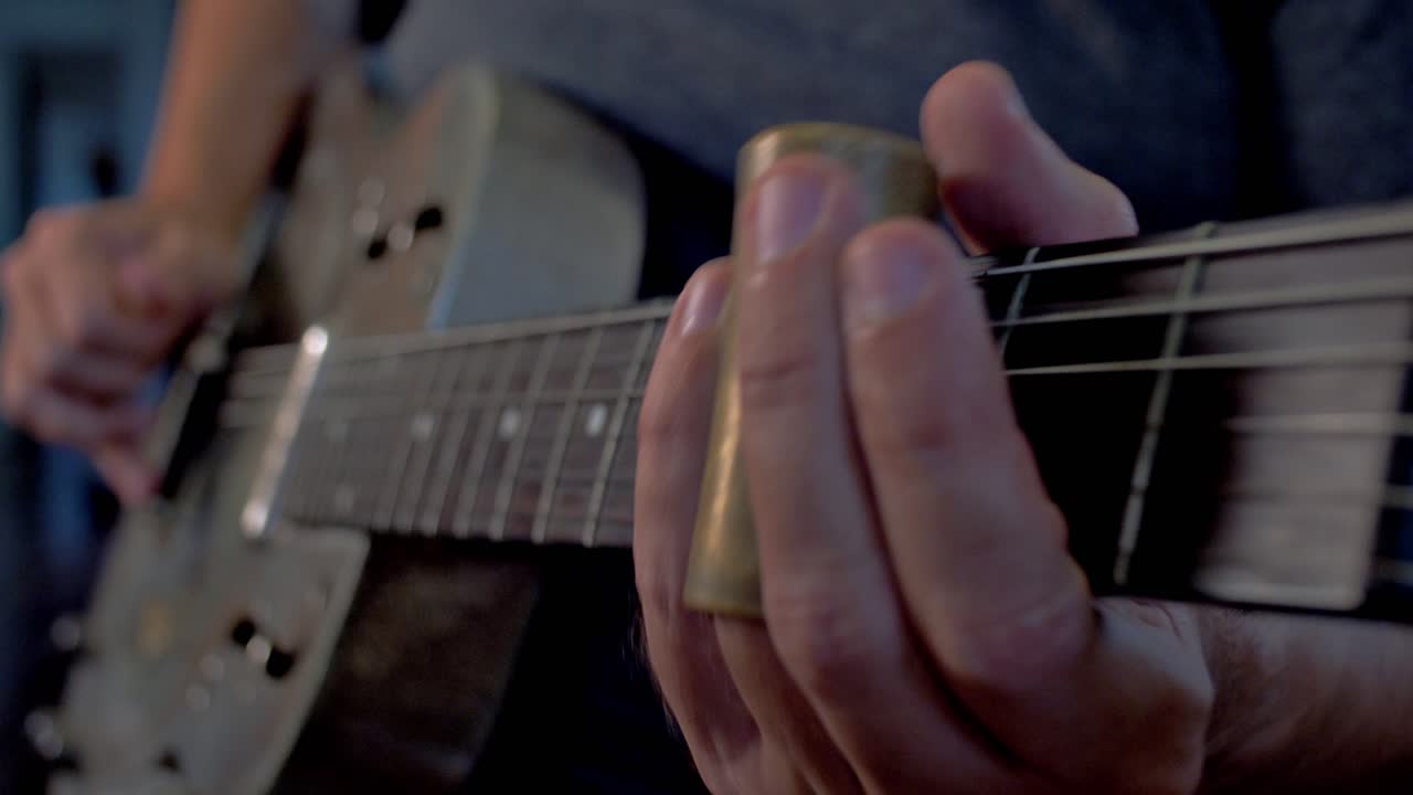 hombre tocando una vieja guitarra resonadora metálica con tobogán cerca del cuello