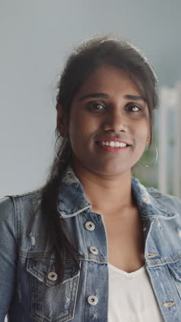 friendly indian woman with ponytail looks in camera smiling. portrait of attractive brunette lady standing in room on blurred background closeup