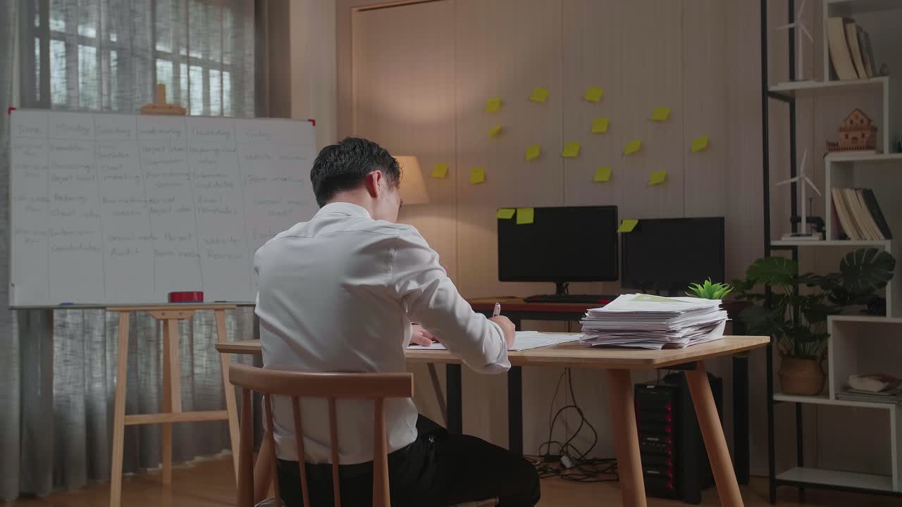 vista trasera de un hombre asiático escribiendo algo en papel mientras trabaja con documentos en la oficina