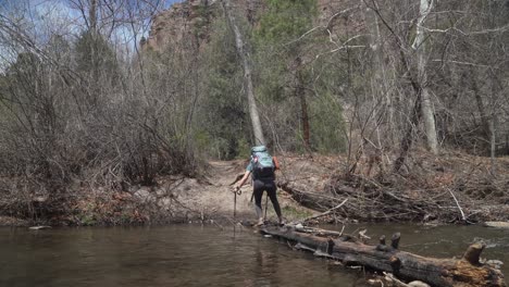 female backpacker carefully crosses stream on log while hiking in new mexico