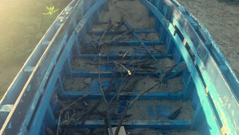 an aged fishing boat resting in a coastal locale, partly buried in the sand with remnants of wooden branches, evoking the quaint aesthetics of a fishing village scene