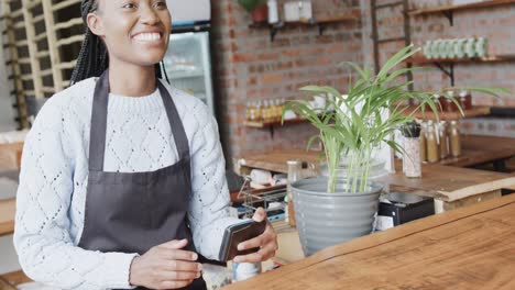 Barista-Afroamericana-Sonriente-Recibiendo-Pago-Por-Reloj-Inteligente-En-La-Cafetería,-Cámara-Lenta