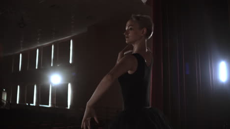 slow motion: prima ballet rehearses a solo performance standing on the stage of the theater in smoke in a black dress in the light.