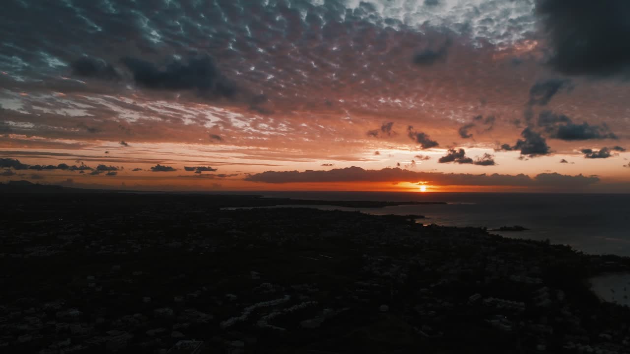 Sweeping, rotating aerial view creating a panoramic sunset over the dark coastline and cityscape of Mauritius. Concept of tropical travel, island sunsets, and wide scenic vistas