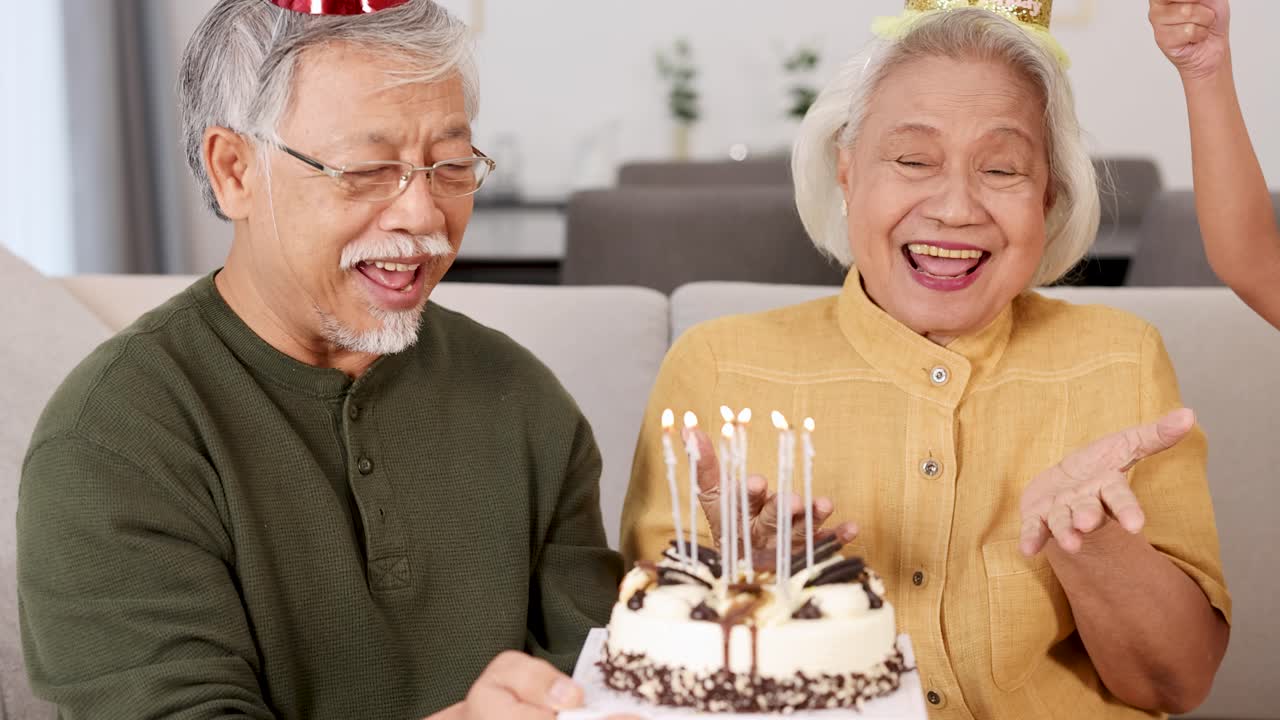 An elderly couple enjoys a birthday celebration with cake and candles in a cozy home setting, filled with laughter and joy