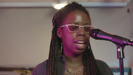 African-american-female-vocalist-singing-and-playing-synthesizer-during-rehearsal-in-recording-studio-with-her-band