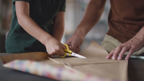 child and father wrapping a gift together