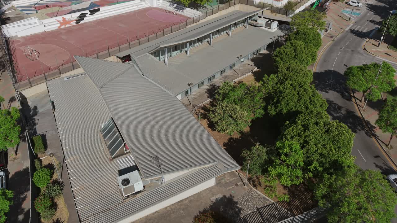 Aerial view of modern architecture in Carlinda district, Málaga, Spain. Contemporary building surrounded by trees and urban streets, captured on a sunny day. Concept of urban design and structure