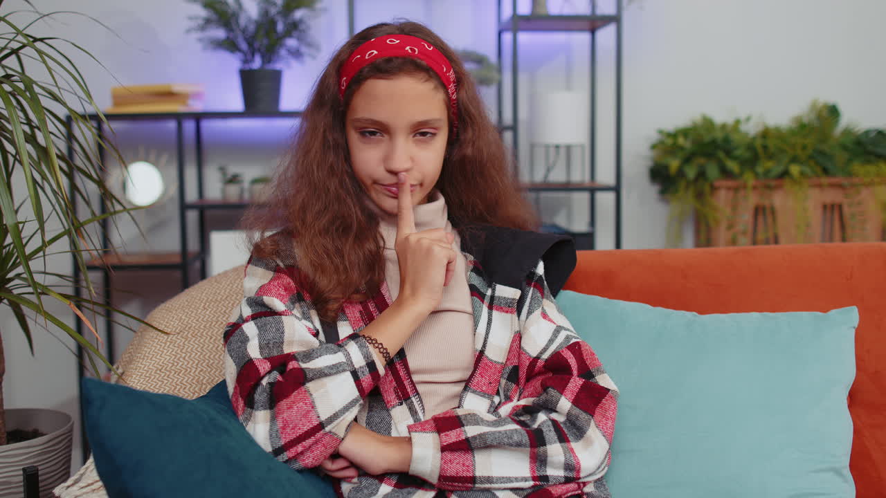 Young girl presses finger to lips makes silence hush sign do not tells gossip secret, quiet at home