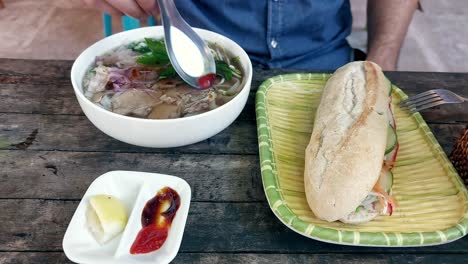 overhead view of adding condiments to a bowl of pho bo or vietnamese beef noodle soup showing the authentic local cuisine of vietnam