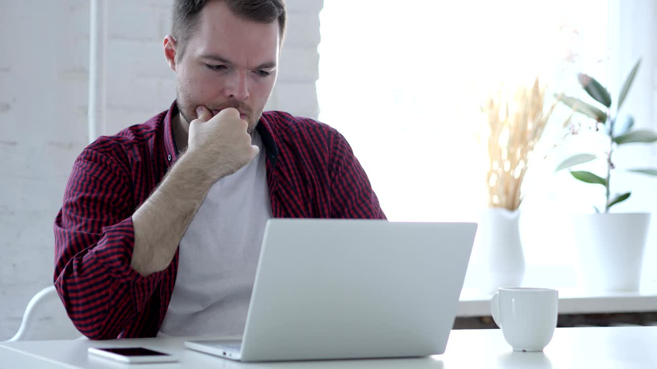 joven pensativo pensando y trabajando en una computadora portátil