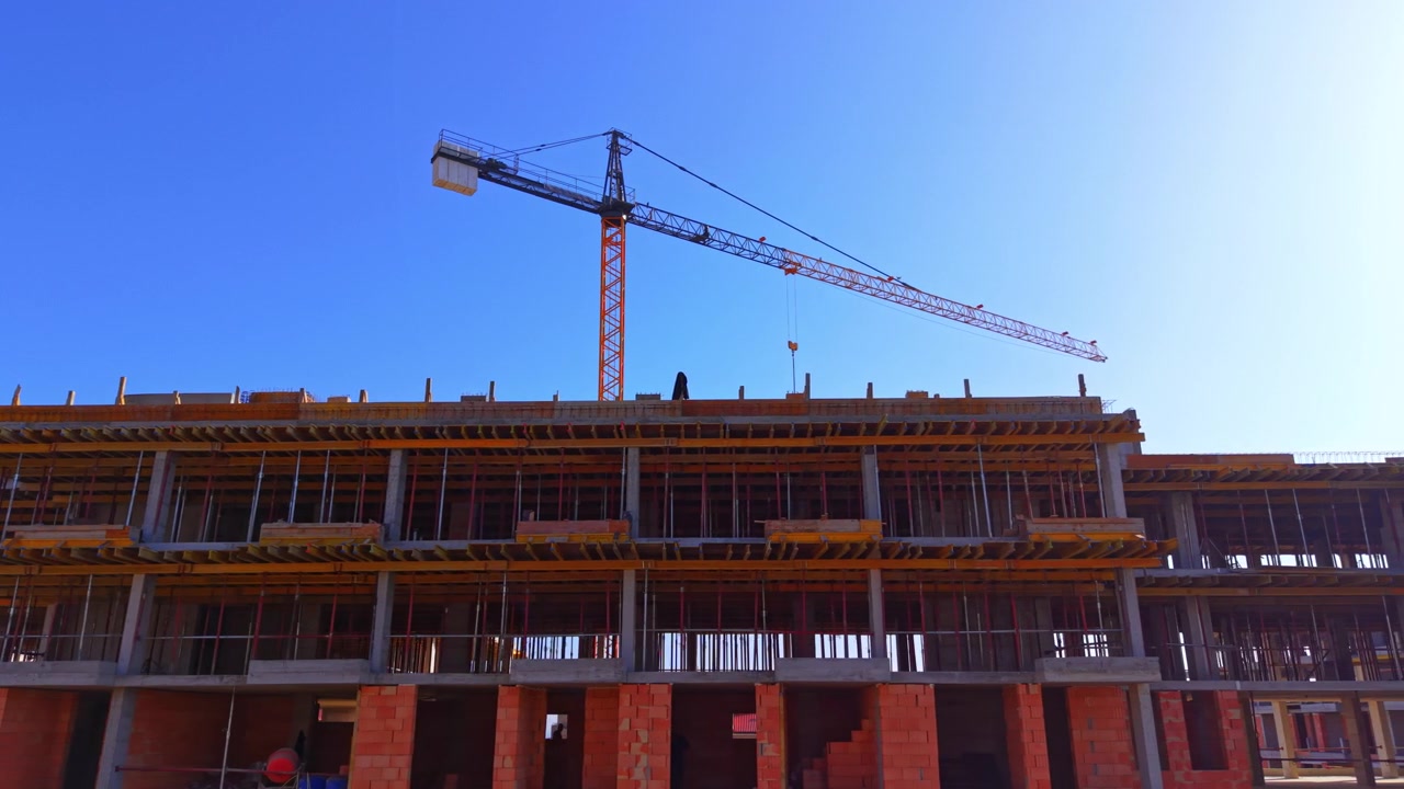 Looking up at a residential structure under development showcasing scaffolding poles and orange brickwork. Aerial view of tower crane above concrete building frame