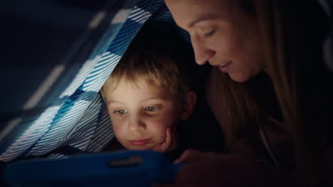 Madre-E-Hijo-Felices-Usando-Una-Tableta-Bajo-Una-Manta,-Un-Niño-Pequeño-Jugando-Con-Tecnología-De-Pantalla-Táctil-Y-Una-Mamá-Relajándose-Y-Divirtiéndose-Antes-De-Acostarse