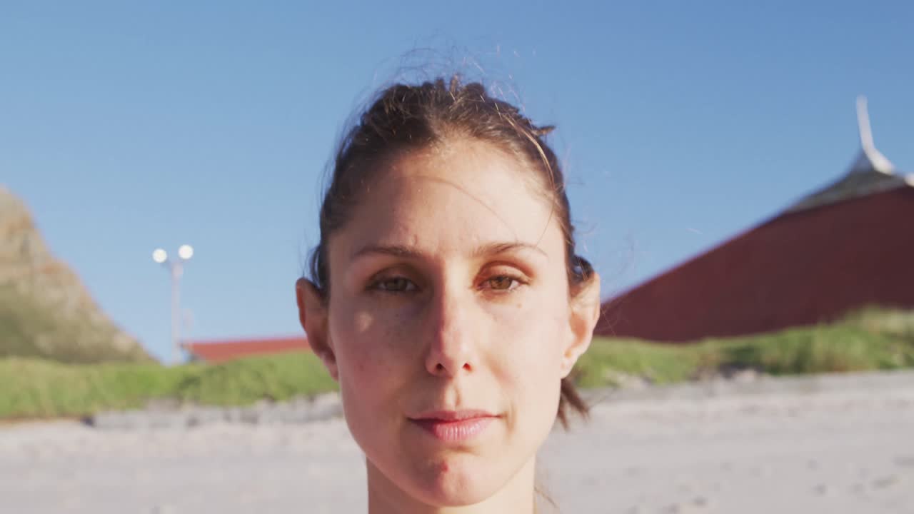 Donna caucasica che guarda la telecamera e sorride sulla spiaggia con lo sfondo del cielo blu.
