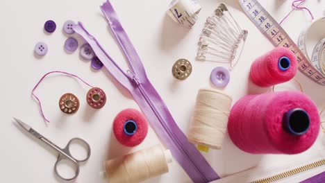 Video-of-tape-measure,-scissors,-safety-pins,-reels-of-thread-and-zips-on-white-background