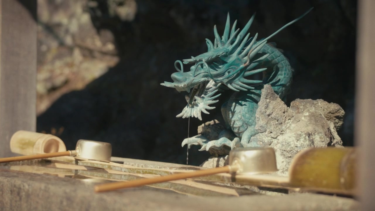 Una statua di drago ornata funge da beccuccio per l'acqua di una vasca di purificazione chōzuya al Santuario Hansobo a Kamakura, parte della tradizione rituale del lavaggio delle mani praticata prima di entrare nei templi giapponesi.
