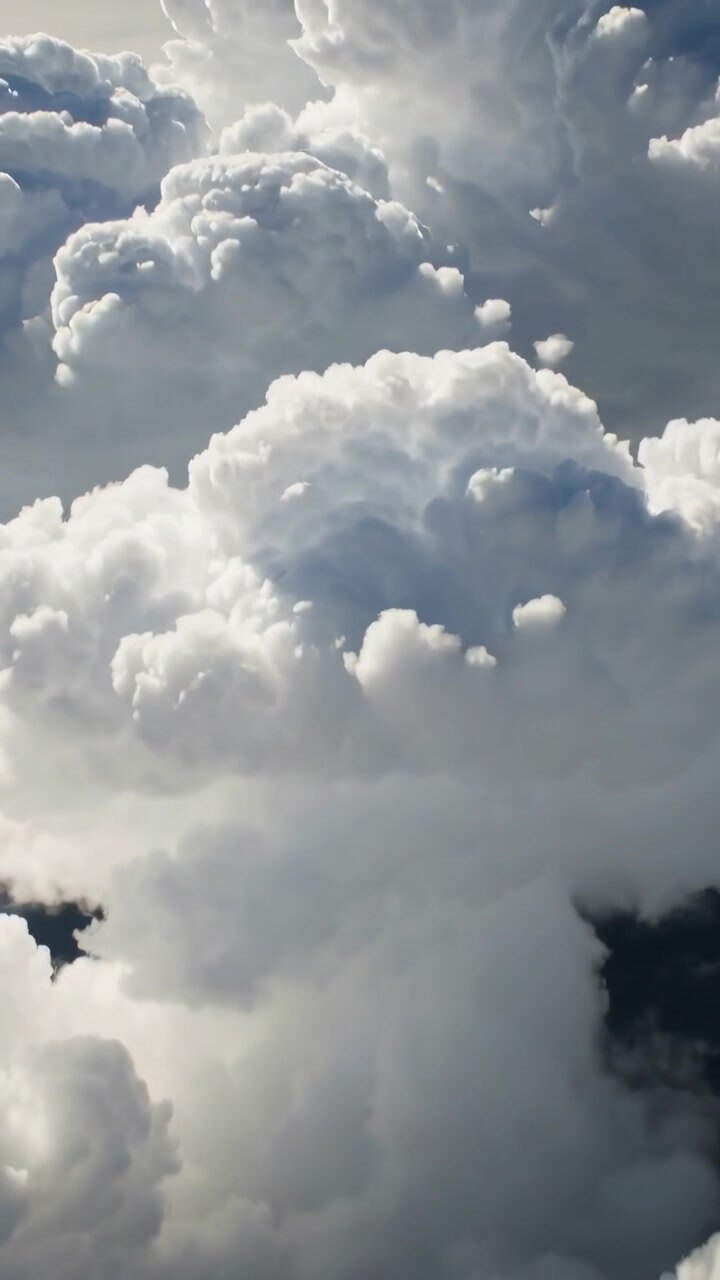 Vertical video: Camera descending over cloud tops, revealing turrets and shadowed cores for weather