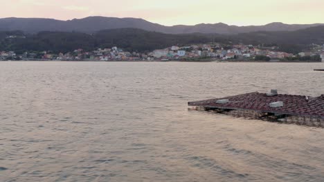 Galizische-Küste-Im-Hintergrund,-Während-Die-Drohne-An-Der-Muschelfarmplattform-Vorbeifliegt