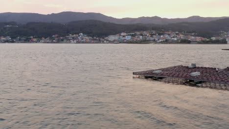 la costa gallega en el fondo, mientras el avión no tripulado pasa la plataforma de la granja de mejillones