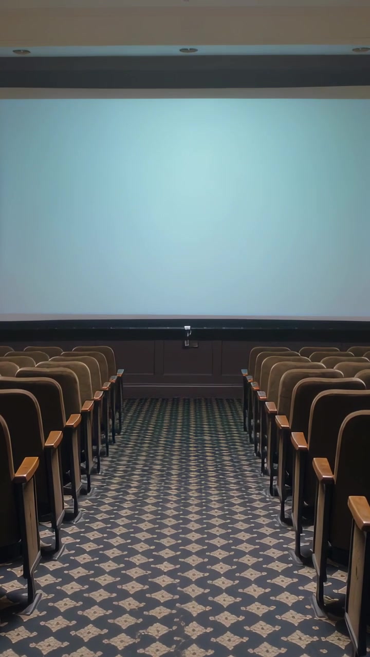 Vertical video: Projector warming, screen shifting from blue to amber over rows of seats in hall