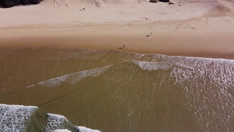 una vista desde arriba de algunas personas y surfistas caminando por la playa en algarve, portugal