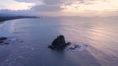 Aerial-tracking-pedestal-up-with-tilt-down-on-lone-limestone-cliff-in-calm-ocean-at-sunset-on-Palawan,-the-Philippines