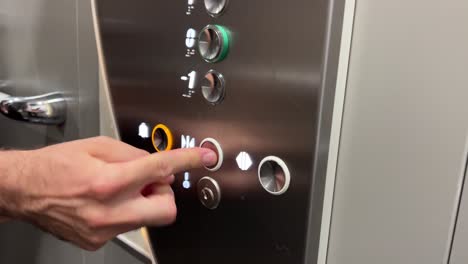 mano caucásica presionando rápidamente el botón de puerta cerrada en un ascensor