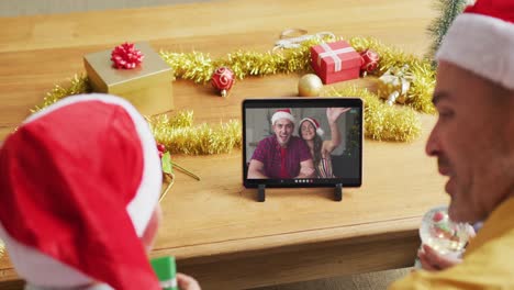 Caucasian-father-with-son-using-tablet-for-christmas-video-call,-with-smiling-friends-on-screen