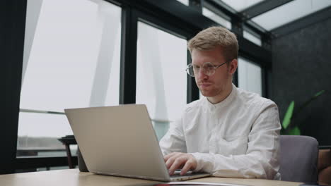 Ernsthafter,-Fokussierter,-Zielstrebiger-Junger-Bärtiger-Geschäftsmann-Oder-Freiberufler-Mit-Brille,-Der-Auf-Dem-Laptop-Tippt-Und-An-Projektrecherchen-Arbeitet,-Indem-Er-E-Mails-An-Den-Kunden-Schreibt