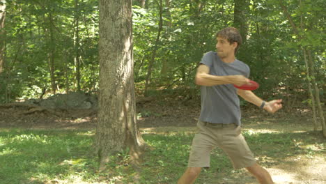 een man die een chauffeur gooit aan het begin van een ronde discgolf in een beboste baan, langzame beweging