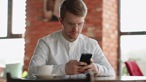 adult attractive man is using smartphone sitting in cafe alone waiting someone and chatting online