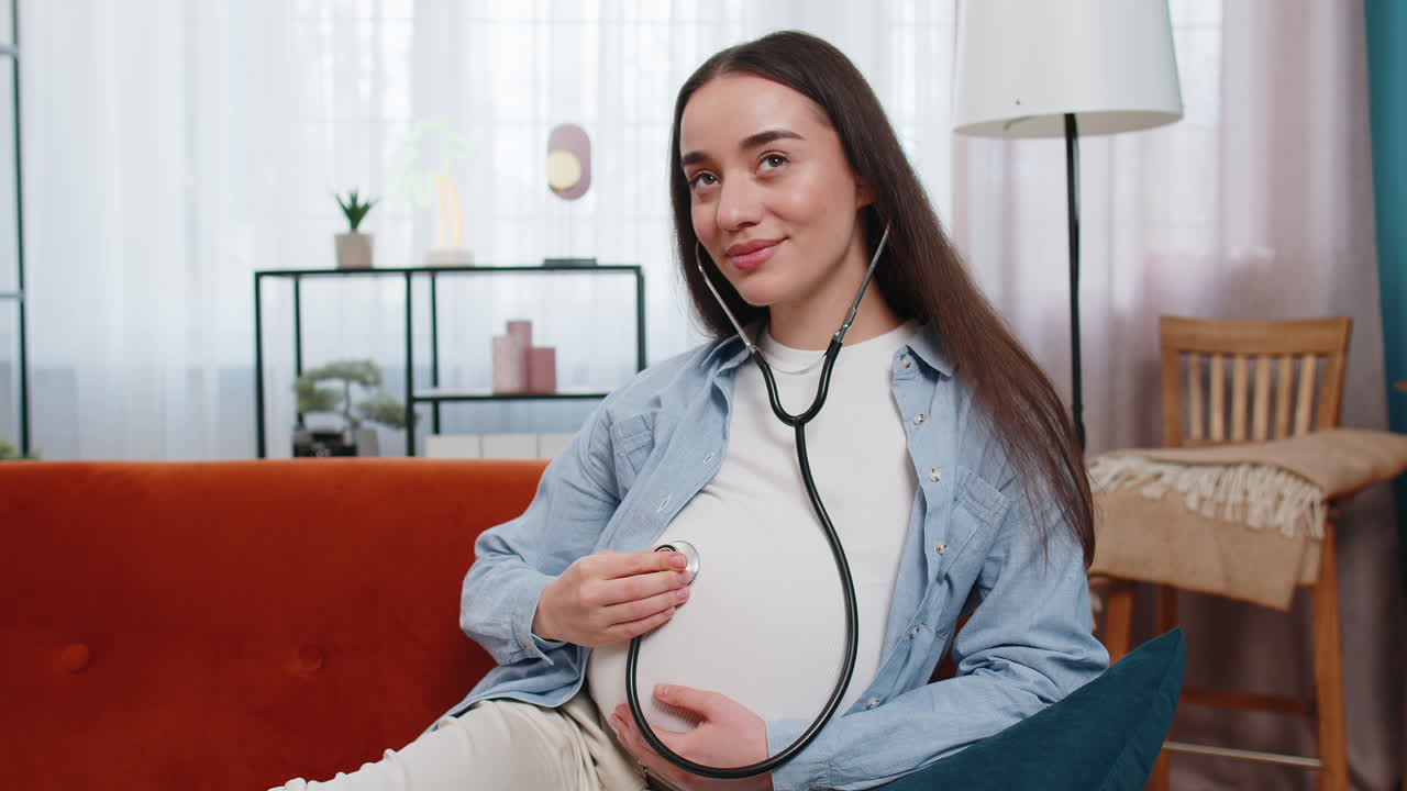 행복 한 임신 한 젊은 여성 은 스테토스코프 를 사용 하여 아기 의 심장 박동 을 듣고 있다.